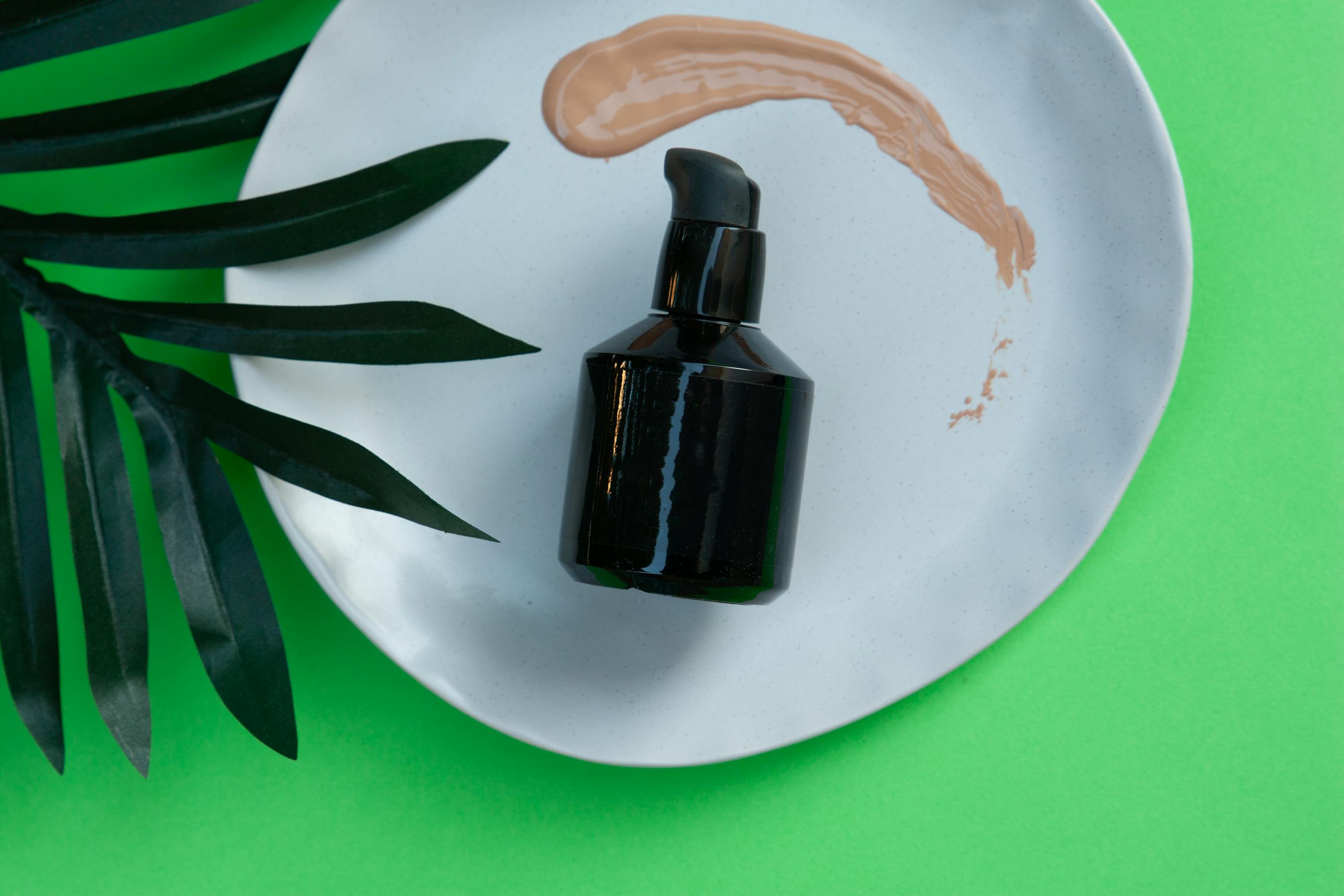 Black skincare pump bottle on white plate with green leaf